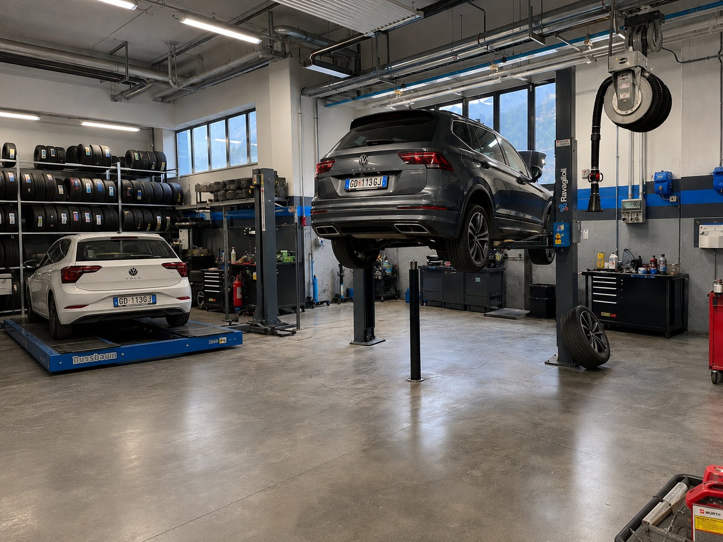Interno dell'officina Cola Srl con Volkswagen Tiguan e Polo sui ponti sollevatori e rastrelliere di pneumatici