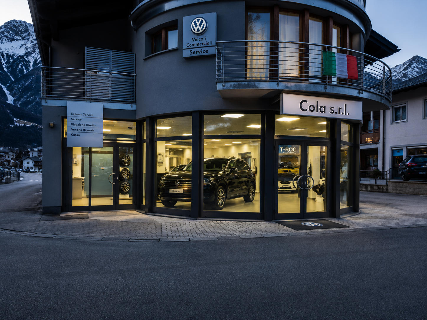 La concessionaria Cola s.r.l. a Bormio al crepuscolo, con showroom illuminato e insegna Volkswagen Service